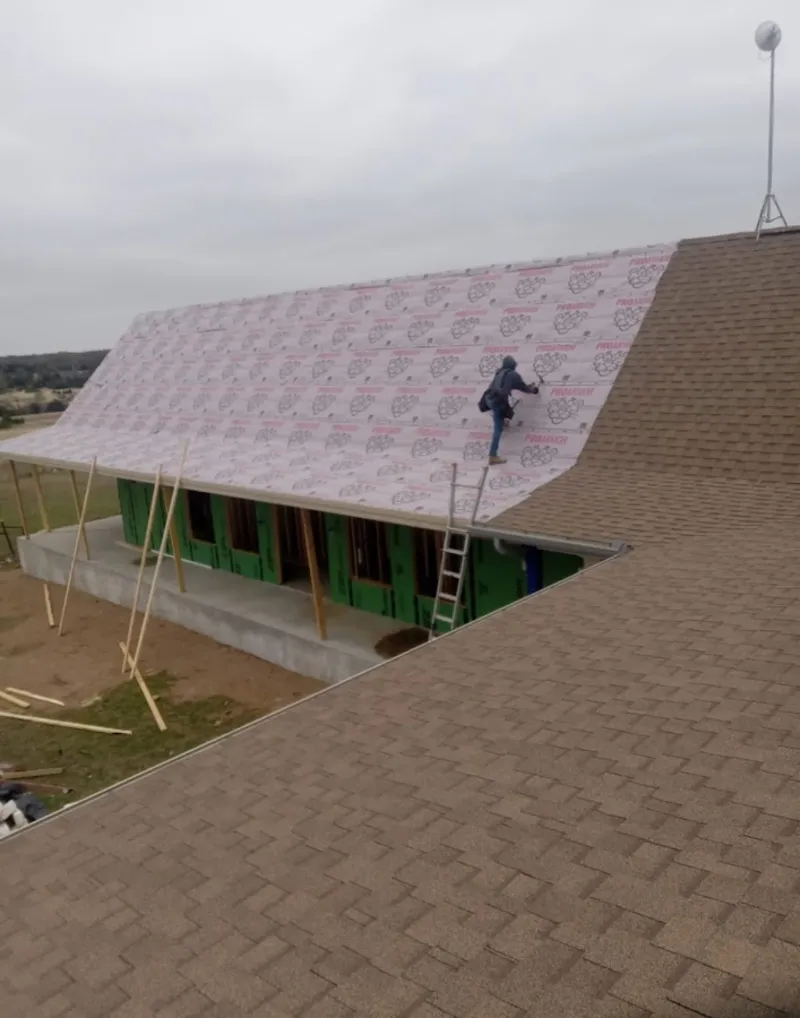 Worker preparing underlayment for a metal roof installation in Clay